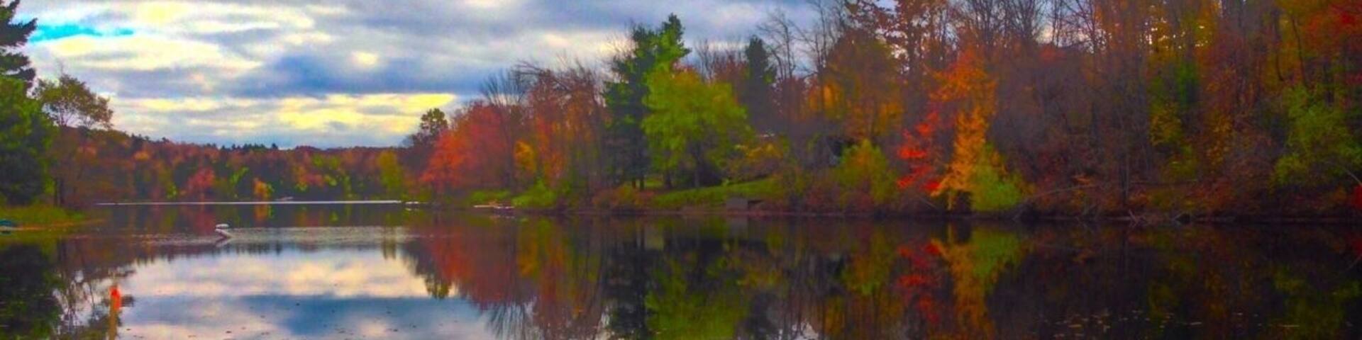 A calm lake surrounded by autumn-colored trees reflecting the sky.