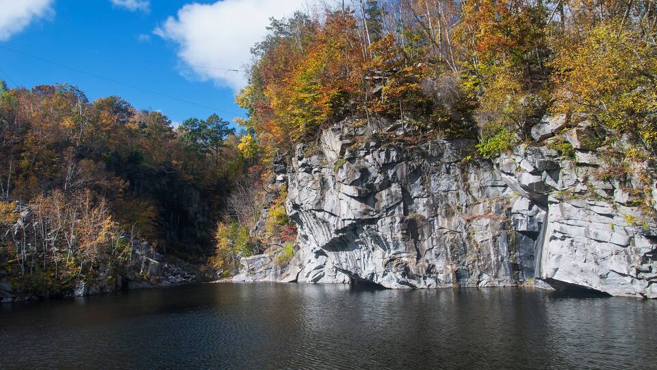 A rocky cliff with autumn foliage beside a calm lake.