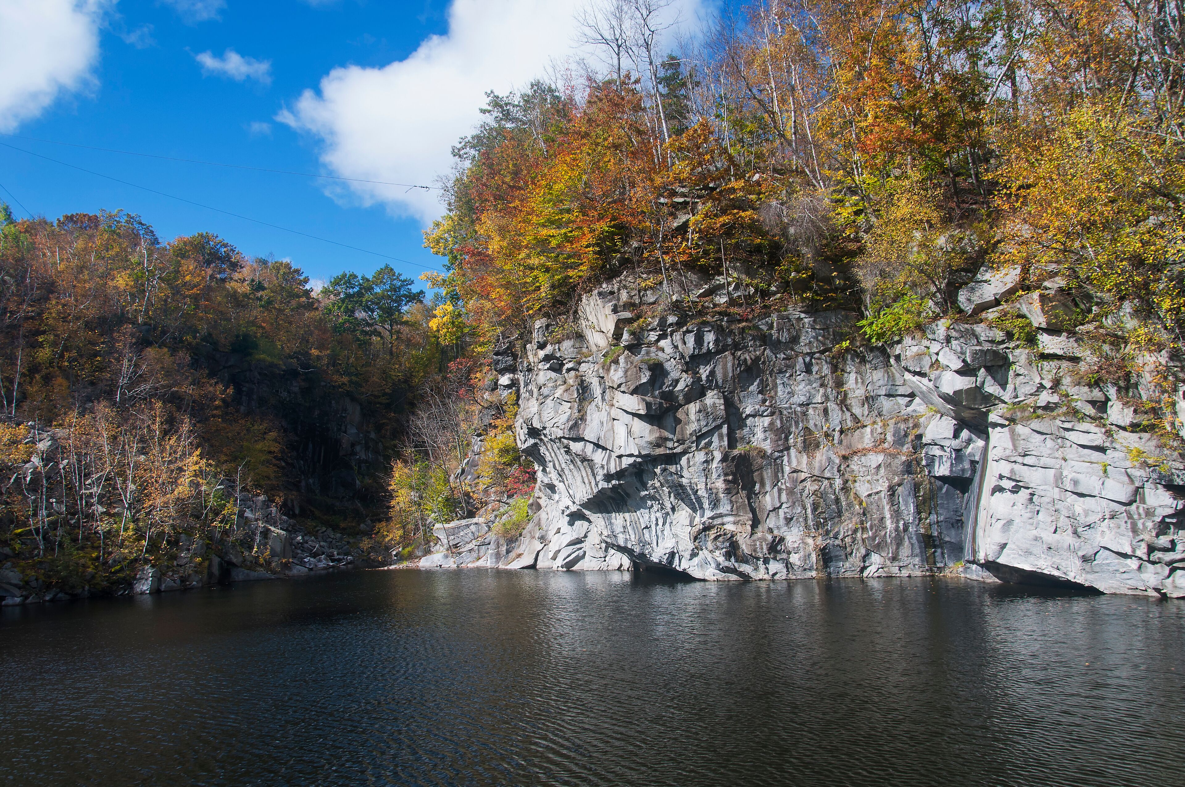 A rocky cliff with autumn foliage beside a calm lake.