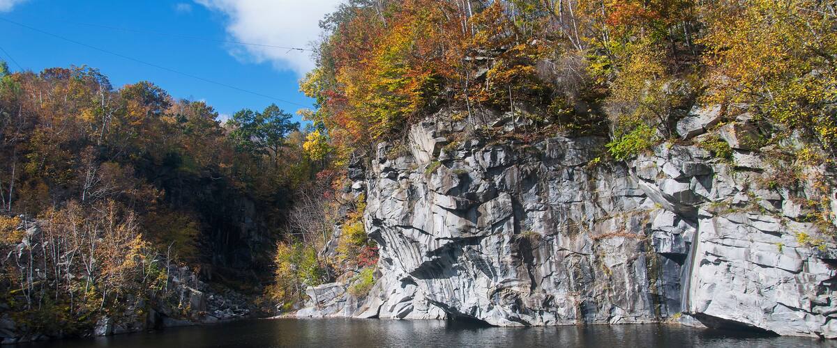 A rocky cliff with autumn foliage beside a calm lake.