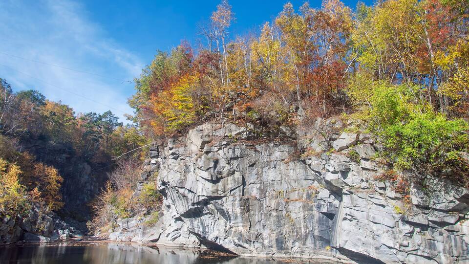 A rocky cliff with autumn foliage and a calm lake.