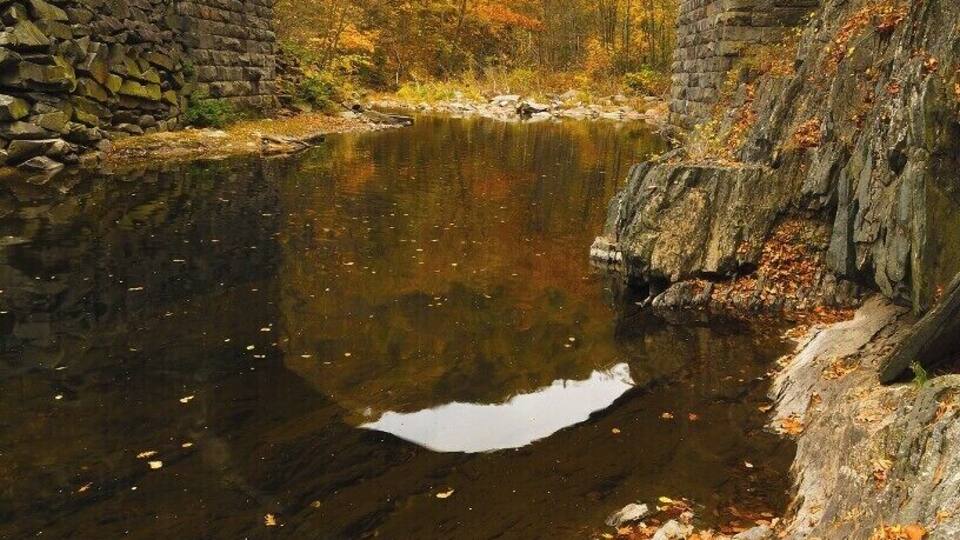 A stone bridge over a calm river with autumn foliage.