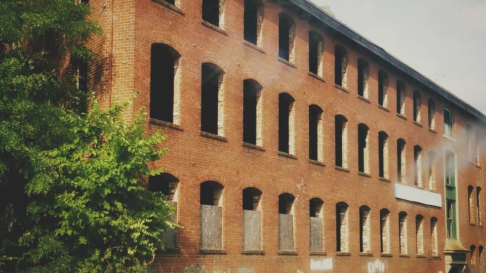 A large, red brick building with multiple arched windows and graffiti on the side.