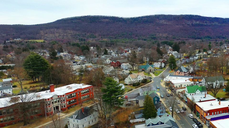 A town with a prominent red building, a green-roofed building, and a hill in the background.