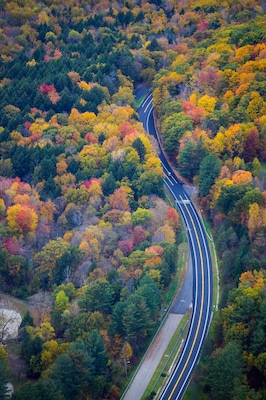A car driving on a road surrounded by fall color in New England - aerial
