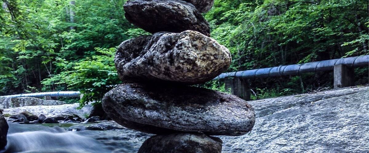 A stack of rocks in a forested area with a waterfall in the background.