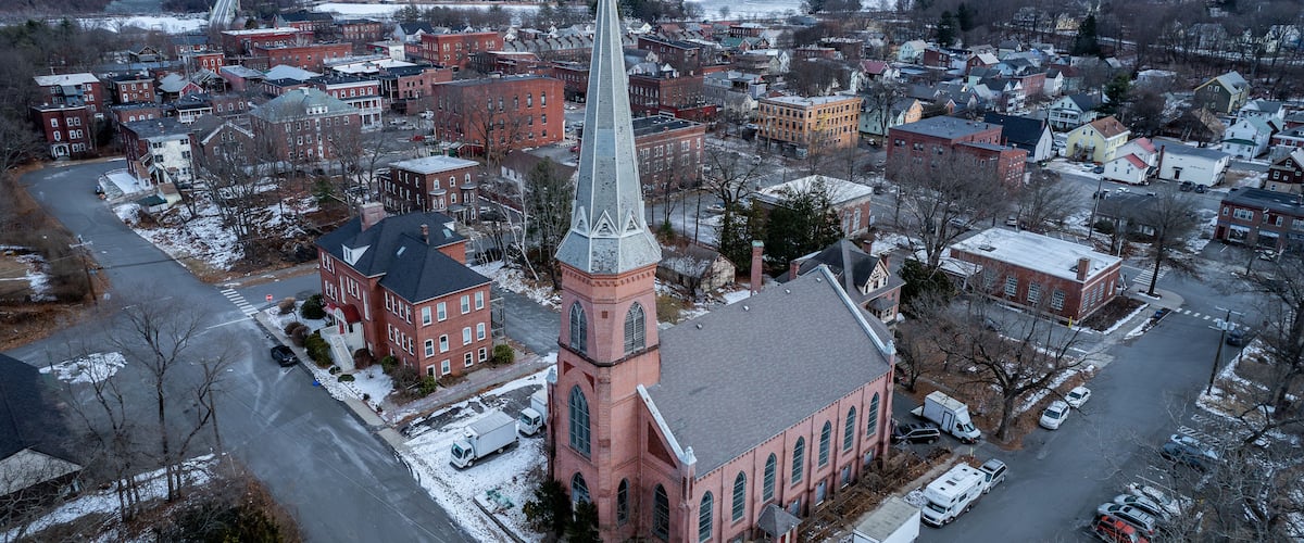 A town with a prominent church featuring a tall steeple, surrounded by residential buildings and a snow-covered landscape.