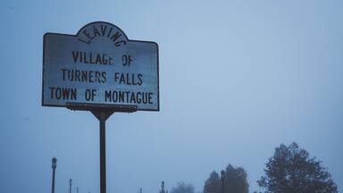 A foggy road with a sign for the Village of Turners Falls, Town of Montague.
