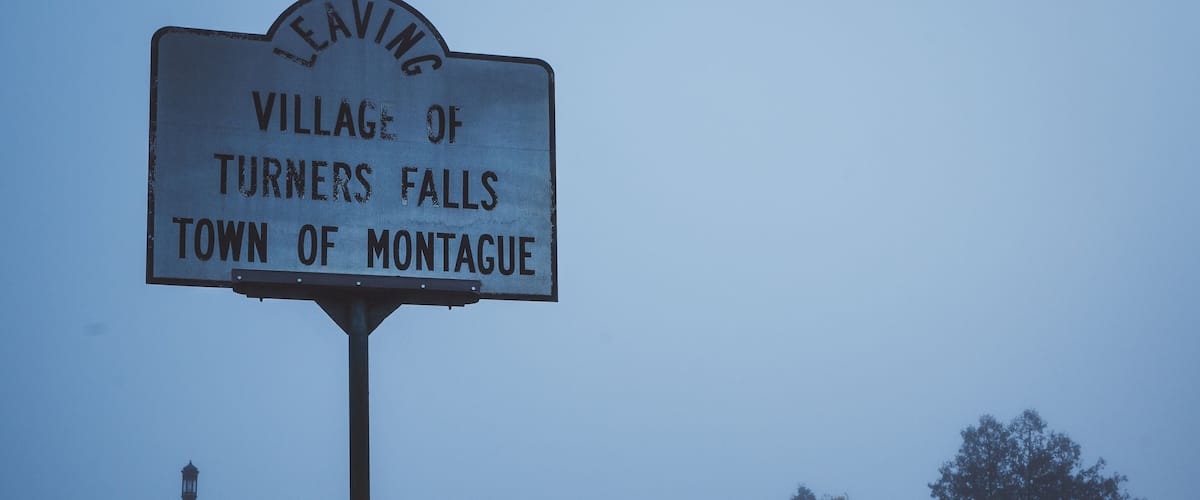 A foggy road with a sign for the Village of Turners Falls, Town of Montague.