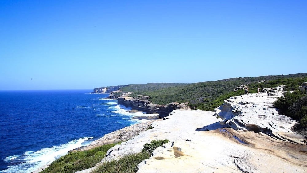 Eine Küstenlandschaft mit schroffen Klippen, blauem Meer und einem grünen Hügelhang.