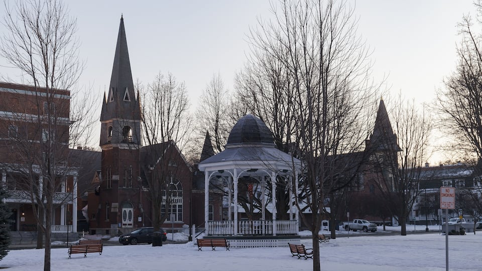 A snow-covered park with a gazebo, benches, and a church with a steeple.