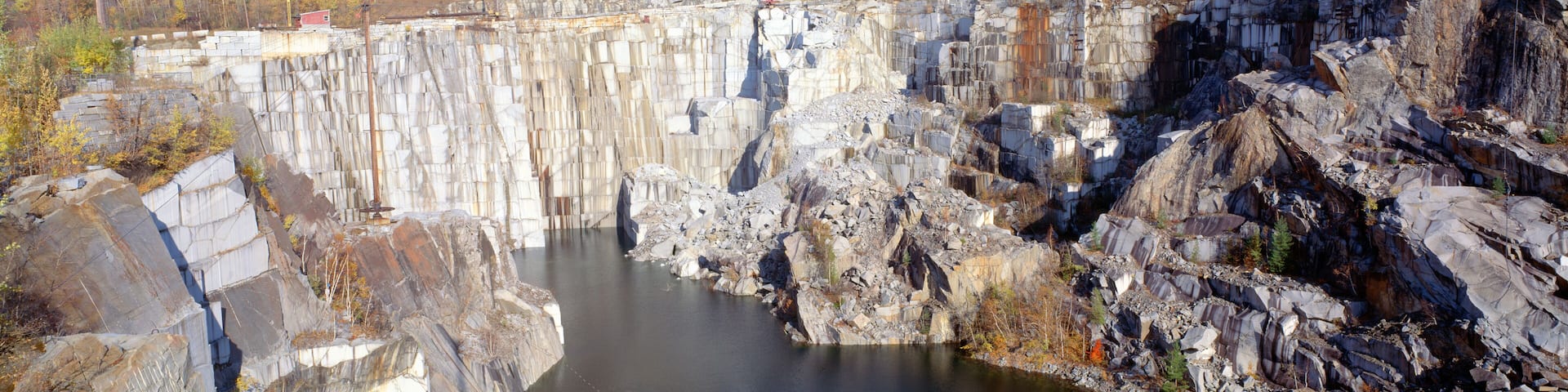A large dam with a reservoir, rocky cliffs, and a forested area in the background.