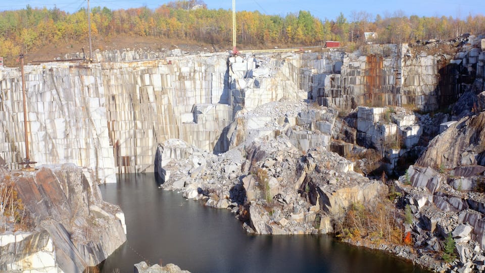 A large dam with a reservoir, rocky cliffs, and a forested area in the background.