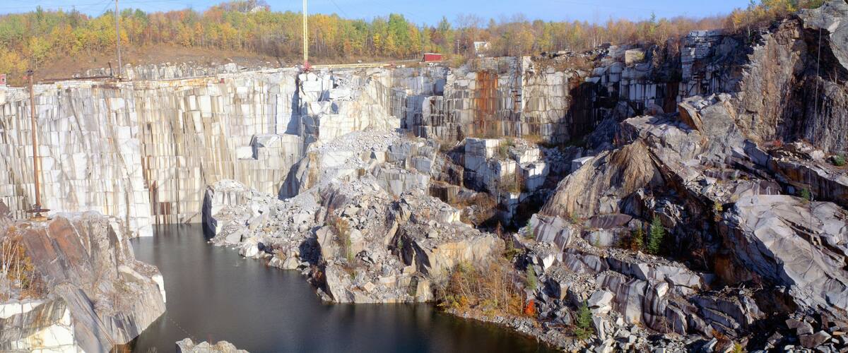 A large dam with a reservoir, rocky cliffs, and a forested area in the background.