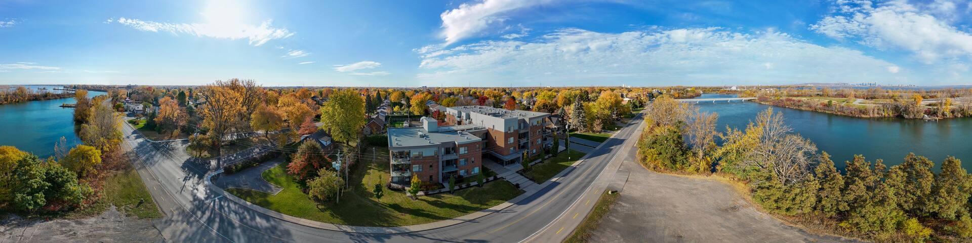 A panoramic view of a residential area with autumn-colored trees, a river, and a bridge.