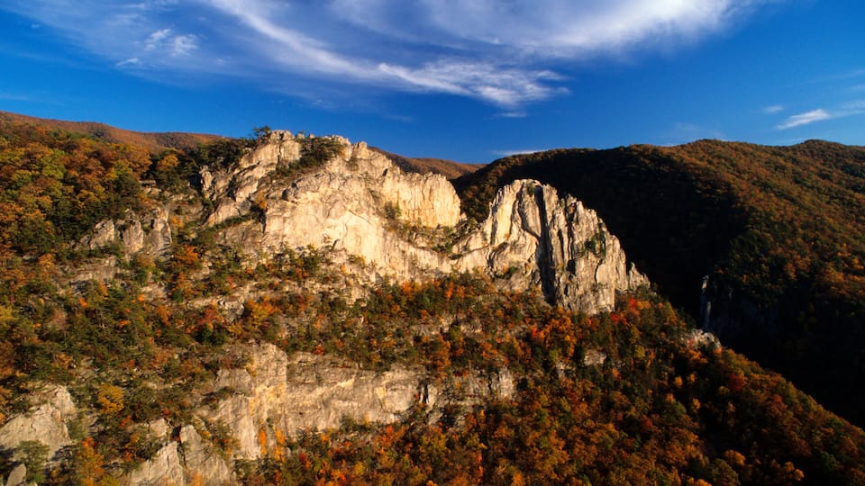 A mountainous landscape with a prominent rock formation and dense autumn foliage.
