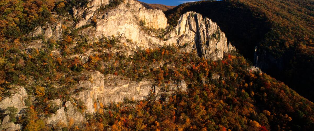 A mountainous landscape with a prominent rock formation and dense autumn foliage.