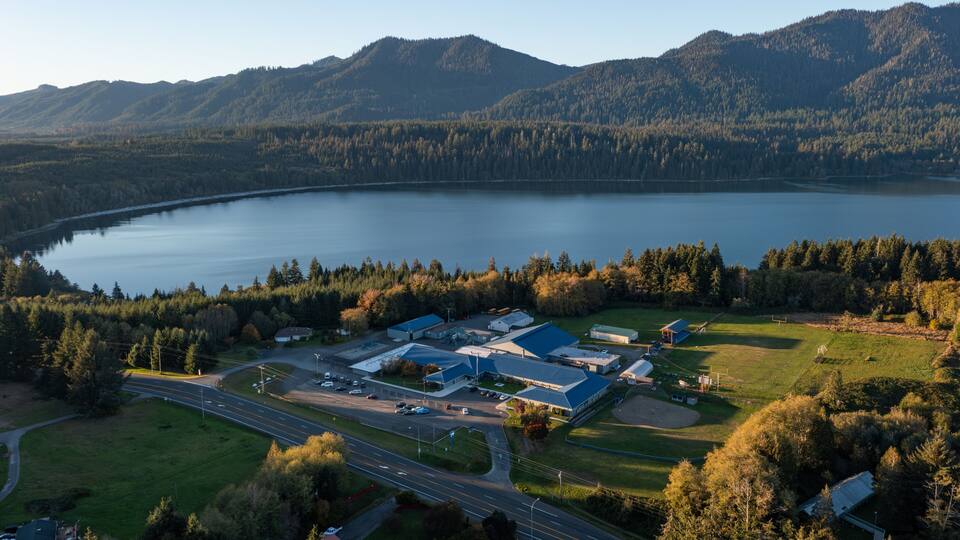 Aerial drone picture of Lake Quinault School District area in Amanda Park, Washington State USA, captured at sunset with warm fall golden light over surrounding evergreen forests and rural landscape