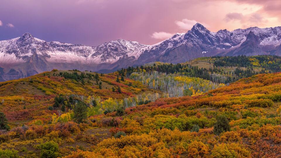 A mountainous landscape with autumn foliage and snow-capped peaks.