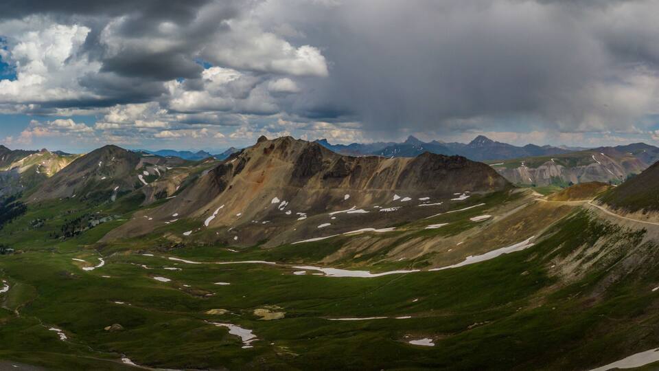 A mountainous landscape with a winding road and patches of snow.