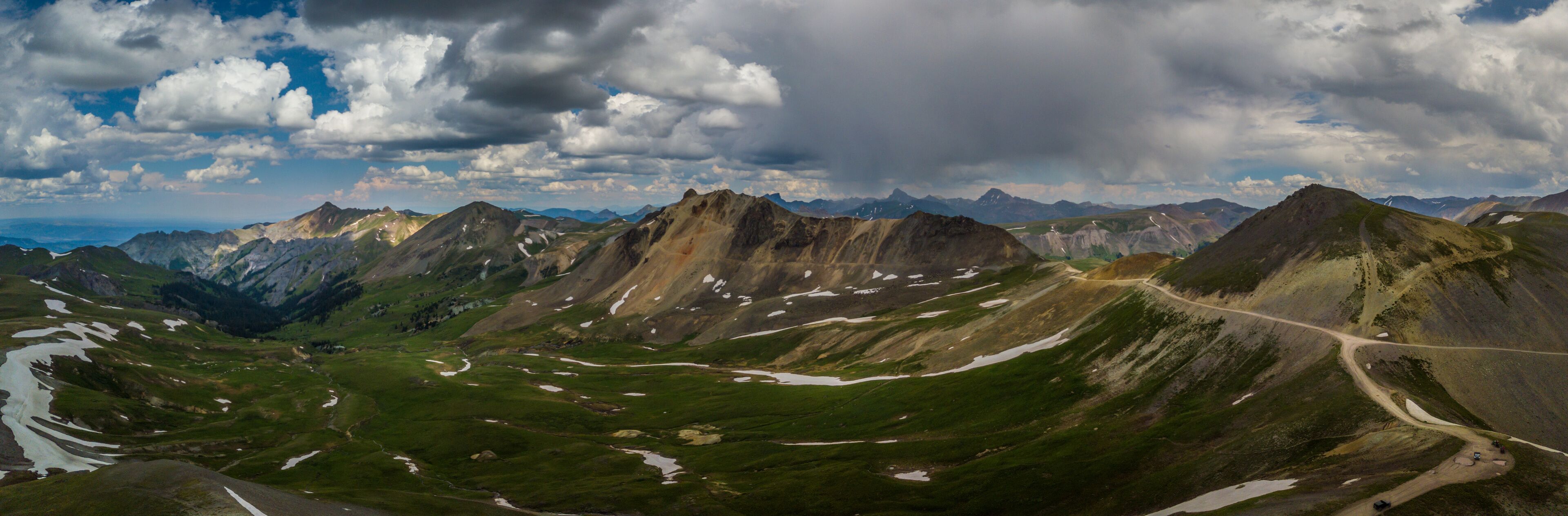 A mountainous landscape with a winding road and patches of snow.