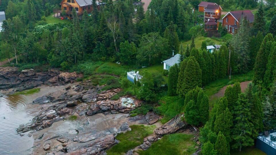 Uma área costeira com margens rochosas, vegetação densa e várias casas de madeira.