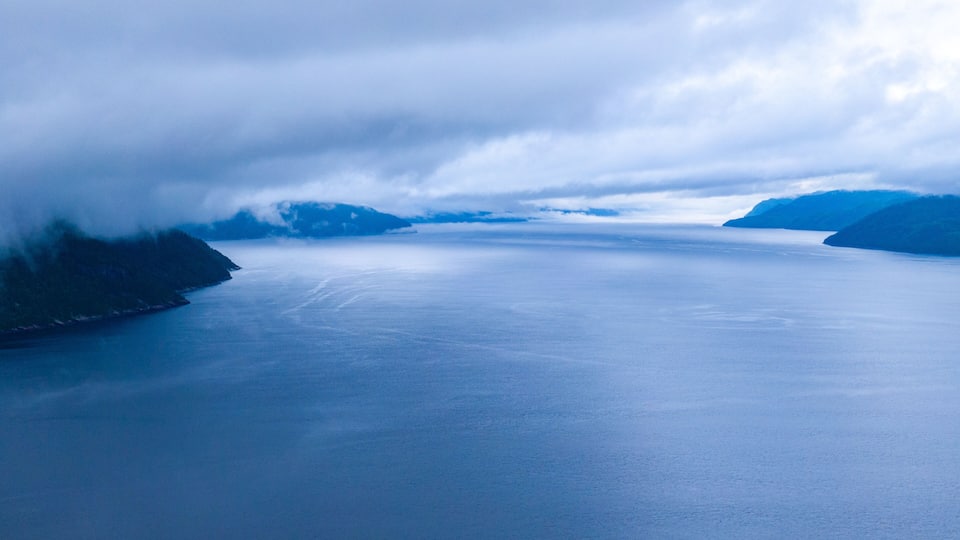 Een rustige zee met bergen in de verte en wolken daarboven.