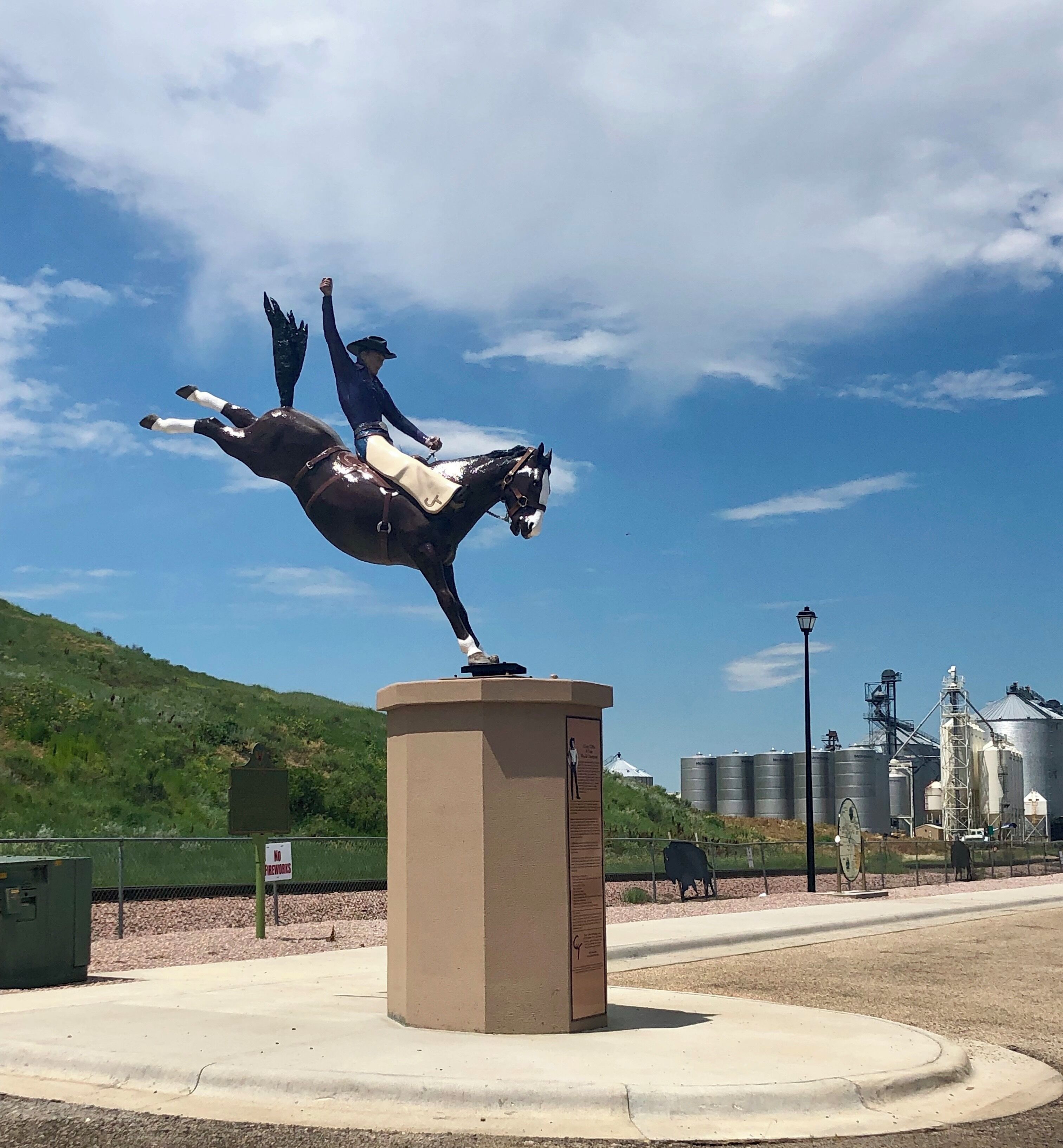 A statue of a person on horseback, a grain silo, and a green hill in the background.