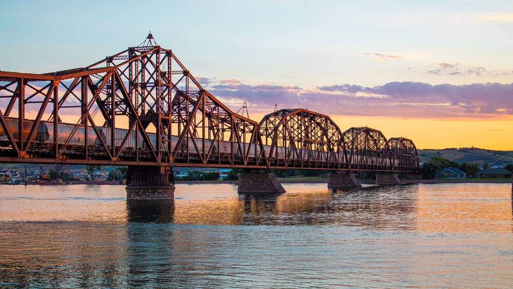 A steel bridge over a river at sunset.