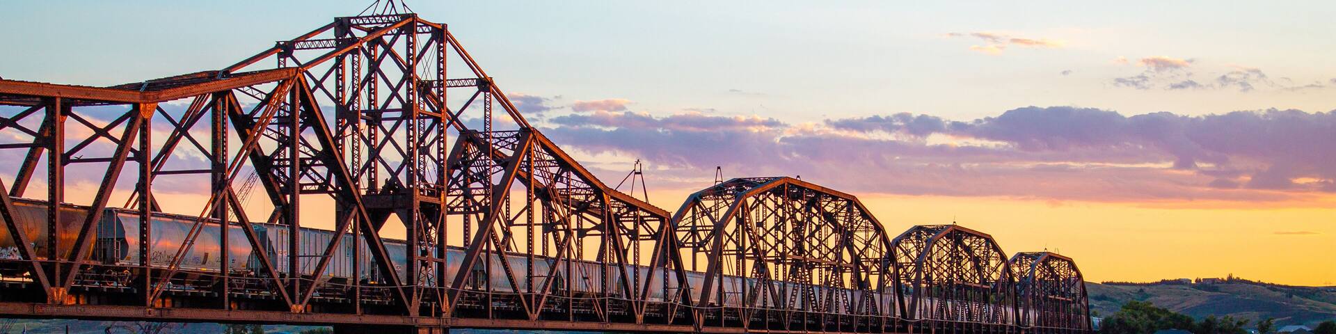 A steel bridge over a river at sunset.