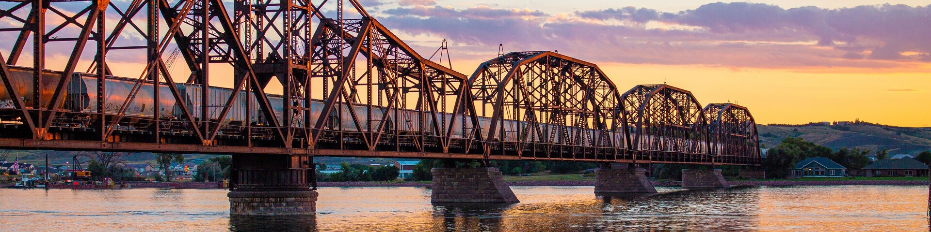 Uma ponte de aço sobre um rio ao pôr do sol.