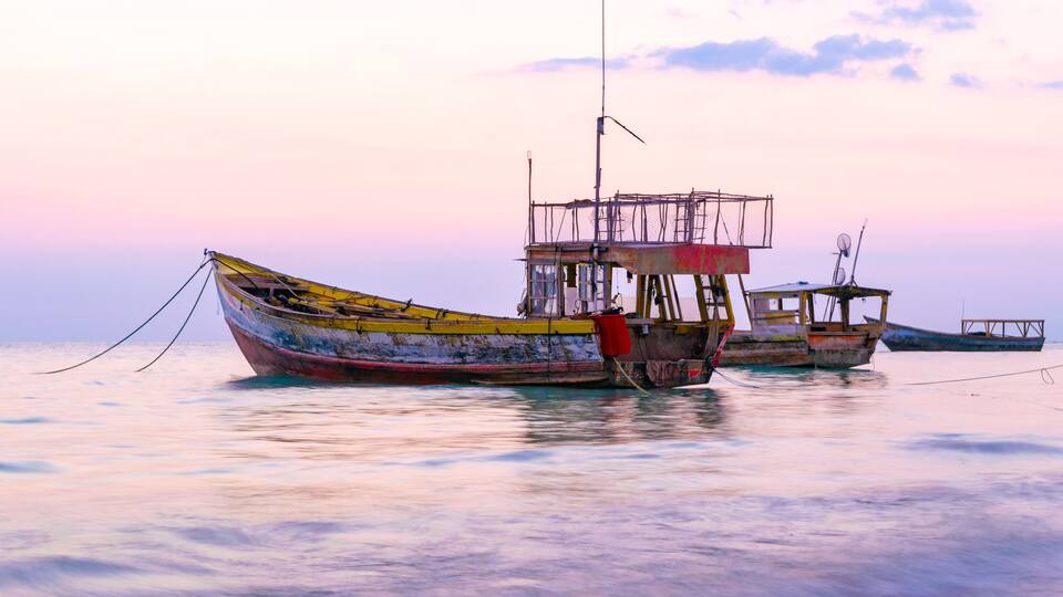 Colorful old wooden fishing boats floating near the coastline at sunset in Westmoreland, Jamaica
