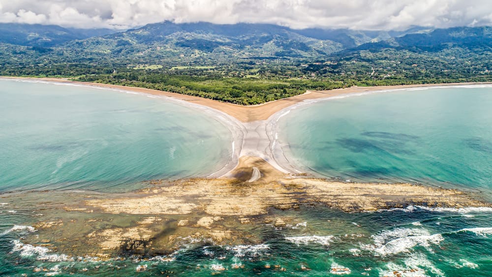 Un paysage côtier avec une baie, des eaux turquoise et limpides, et une chaîne de montagnes en arrière-plan.