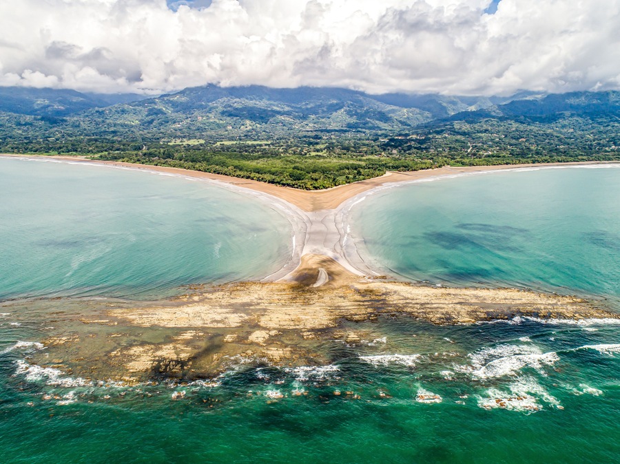 A coastal landscape with a bay, clear turquoise waters, and a mountainous backdrop.