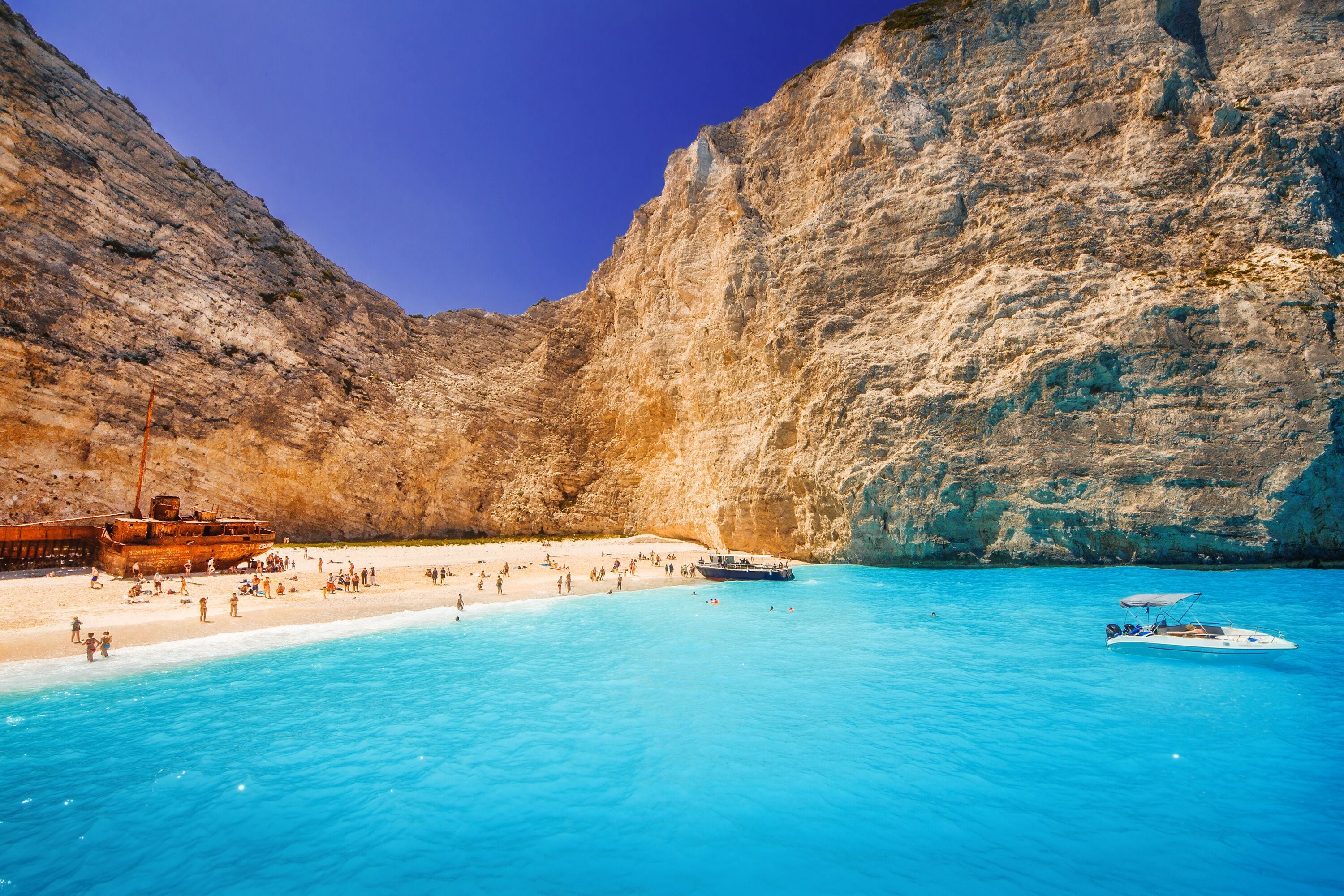 A coastal beach with clear blue waters, a rocky cliff, and a small boat.