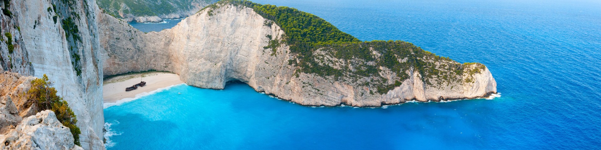 A coastal cliff with a beach and turquoise waters.