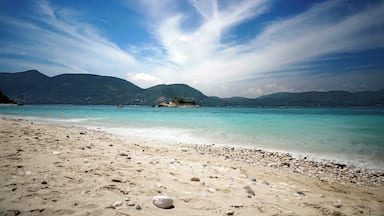 Uma praia com águas turquesa cristalinas, areal de seixos e montanhas ao fundo.