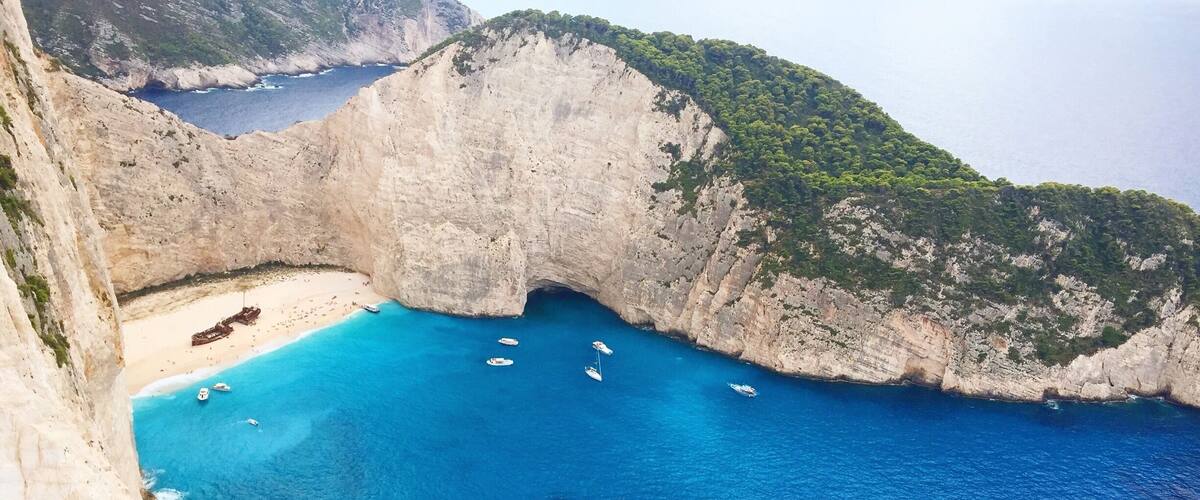 A coastal cliff with a narrow opening leading to a turquoise bay.