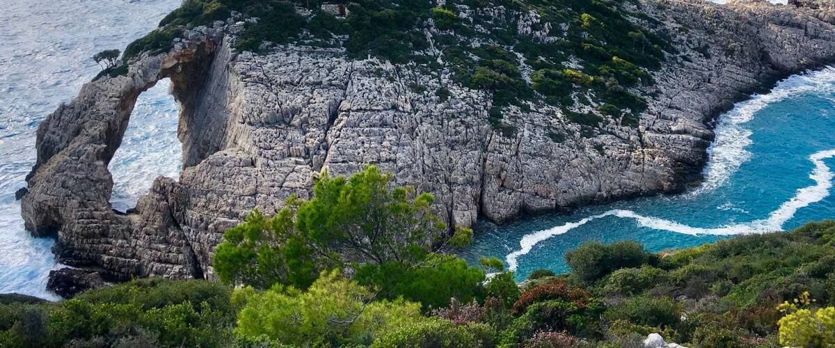 A rocky coastline with a prominent arch formation and lush greenery.