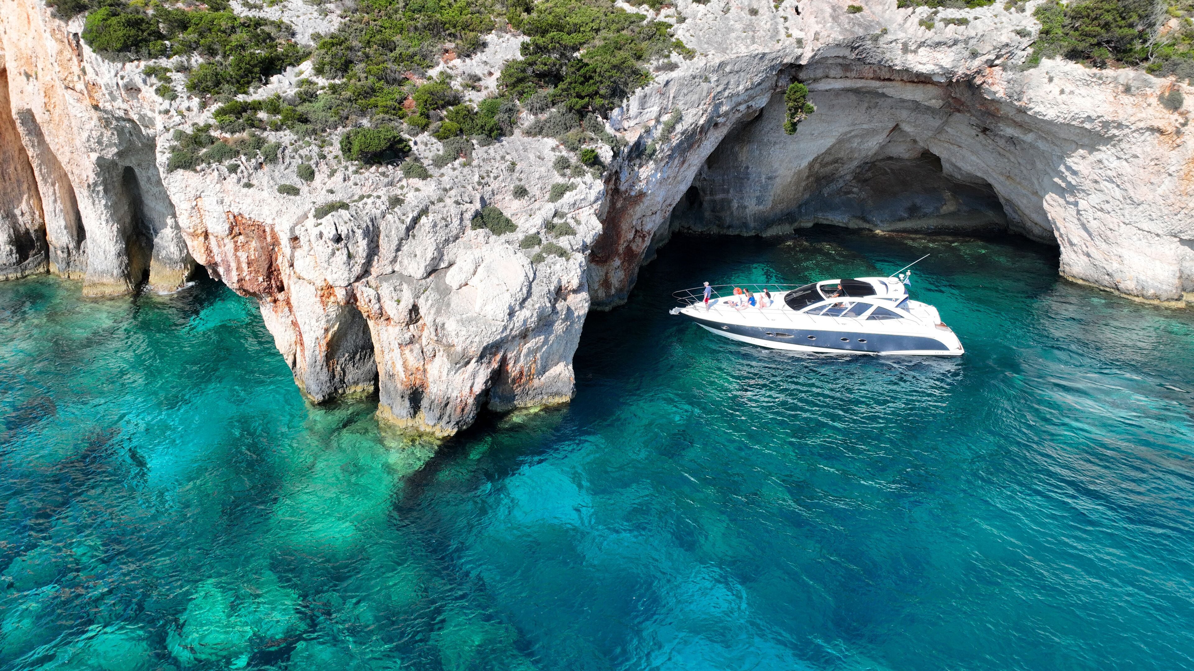 A boat anchored near a rocky coastline with clear turquoise water and a natural arch formation.