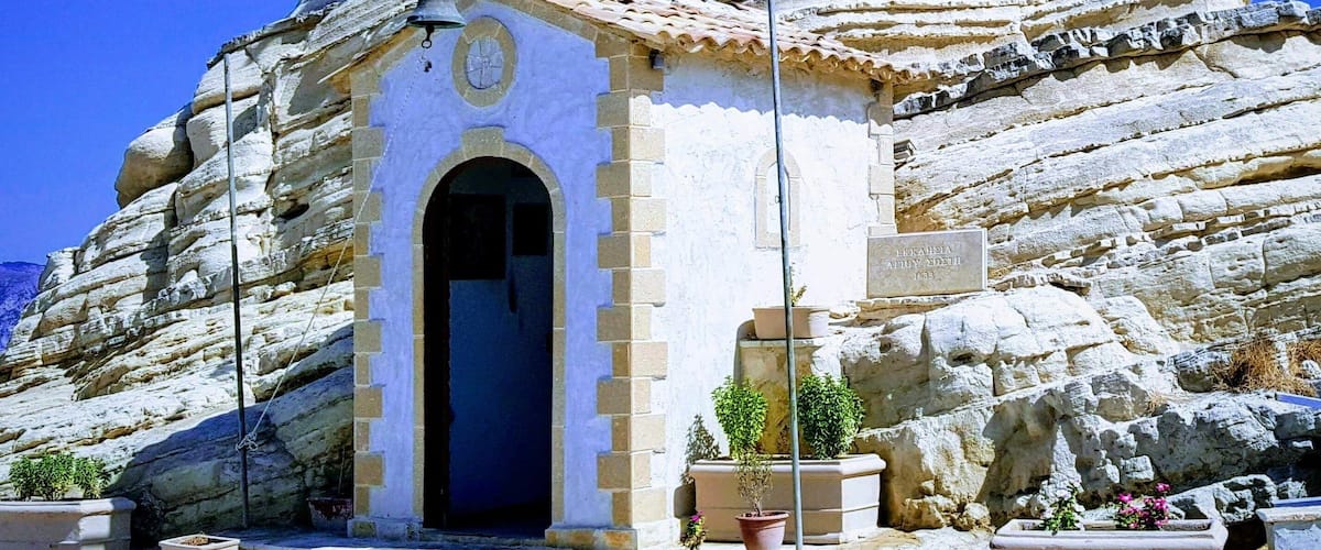 A chapel built into a rocky cliff, with a flag on top and a bell.