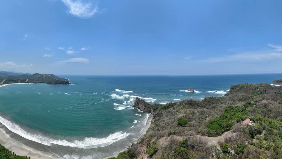 A coastal landscape with a curved beach, rocky outcrops, and dense vegetation.