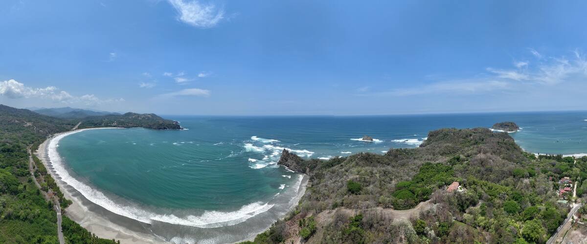 A coastal landscape with a curved beach, rocky outcrops, and dense vegetation.