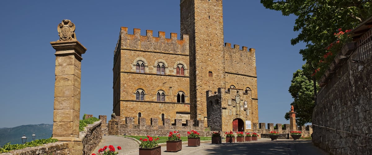 A historic stone castle with a tall tower, arched windows, and a statue on a pedestal.