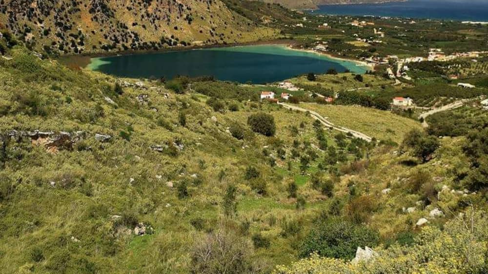 Un paysage côtier avec un lac turquoise, entouré de collines et d’une végétation clairsemée.