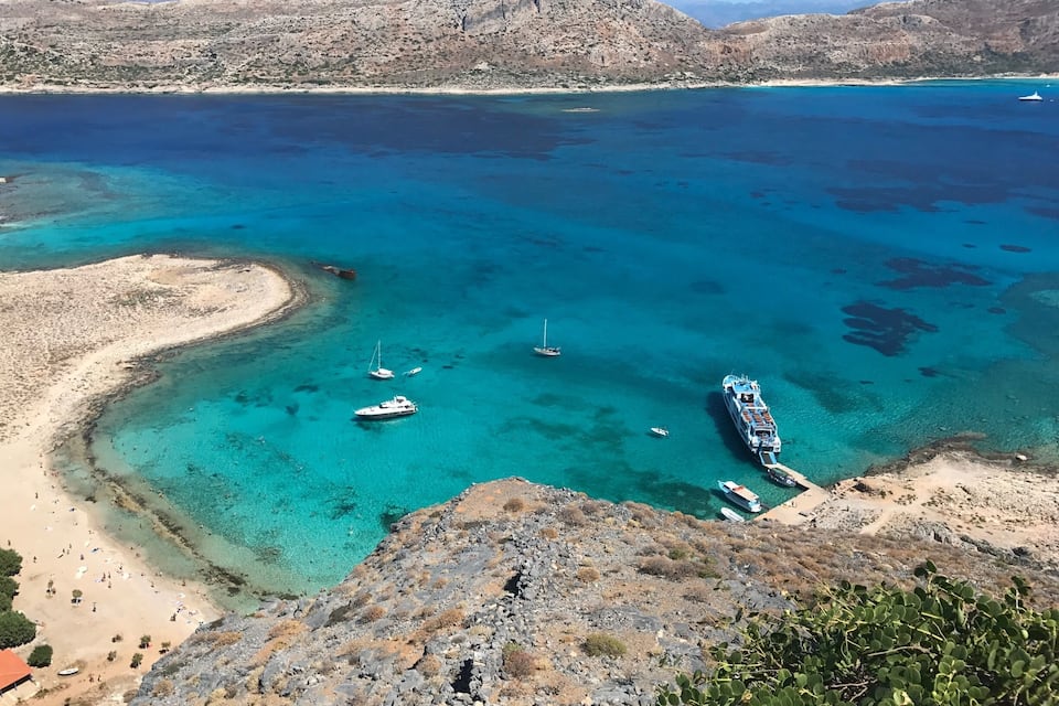 Un paysage côtier caractérisé par une eau turquoise et limpide, un terrain rocheux et quelques bateaux amarrés près du rivage.