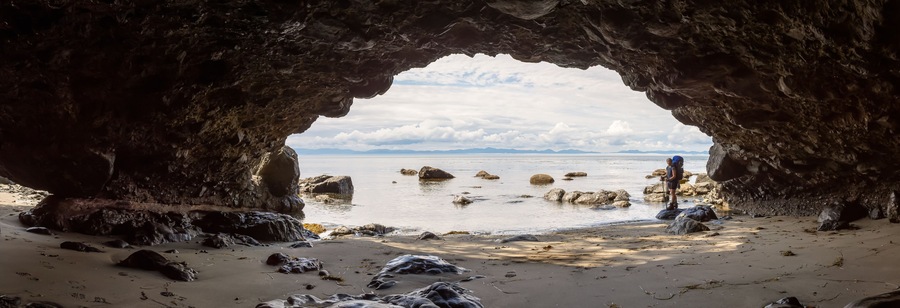 A rocky cave opening to a beach with scattered rocks and a distant mountain range.