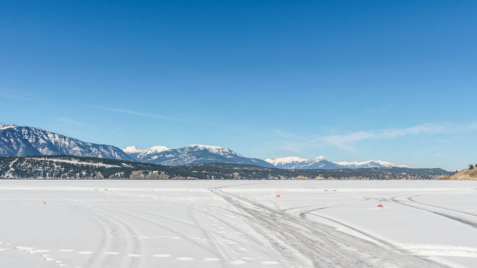 A snow-covered landscape with mountains in the background and tire tracks on the snow.