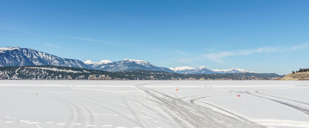 A snow-covered landscape with mountains in the background and tire tracks on the snow.
