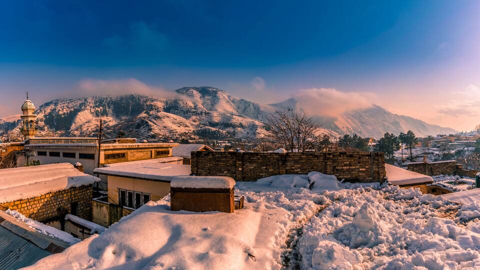 A snow-covered mountainous landscape with a mosque and residential buildings.